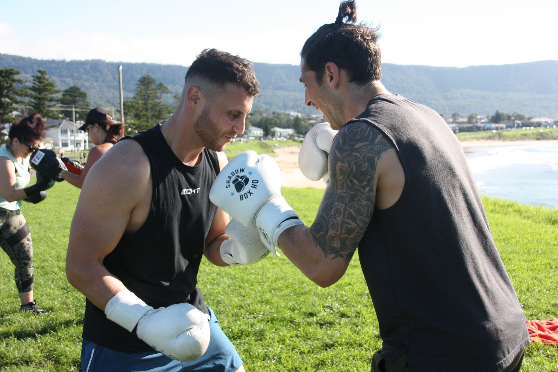 Two men boxing outdoors near the coast, wearing gloves, focused.