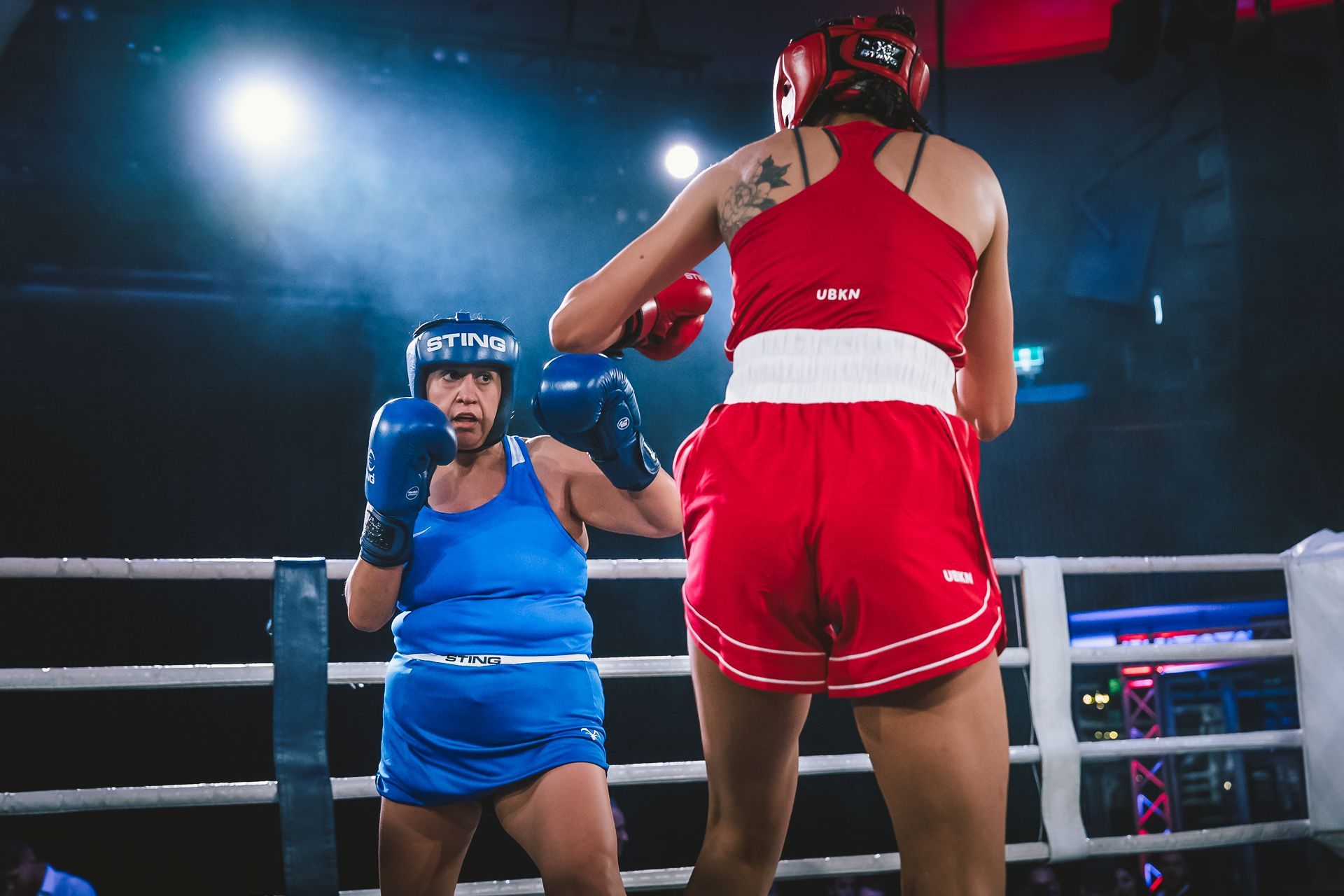 Two boxers in red and blue outfits in a boxing ring, facing each other with gloves up.