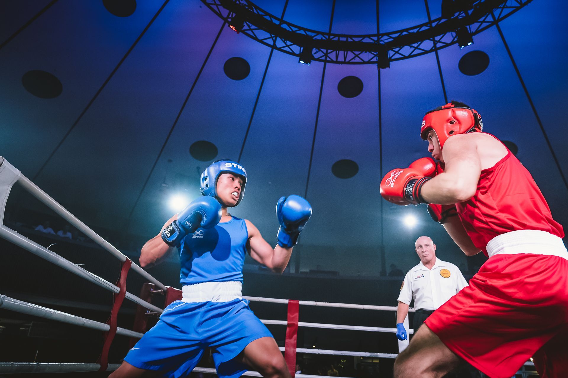 Two boxers in red and blue fighting in a ring, referee watches.