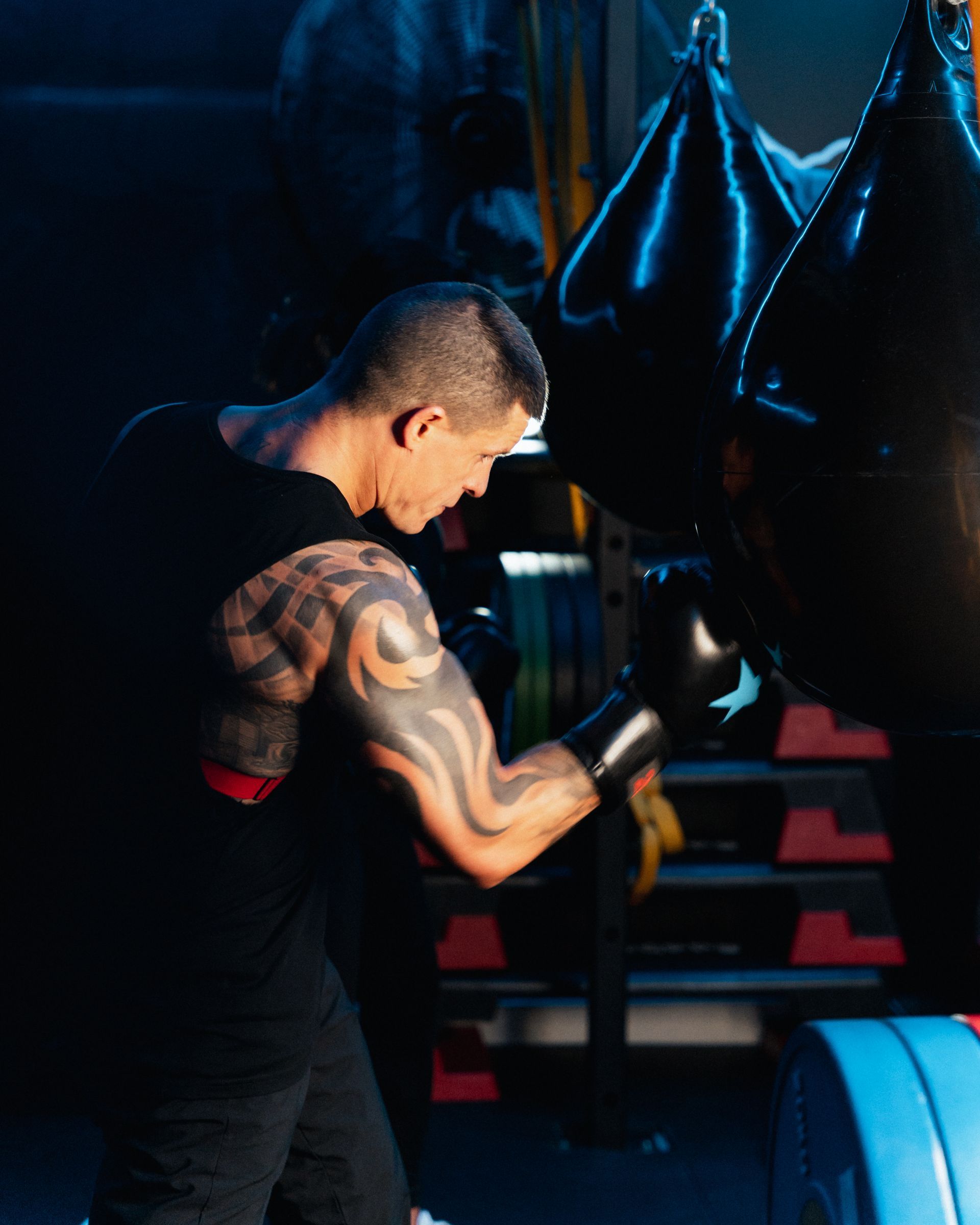Man with arm tattoos boxing a black punching bag in a dark gym.