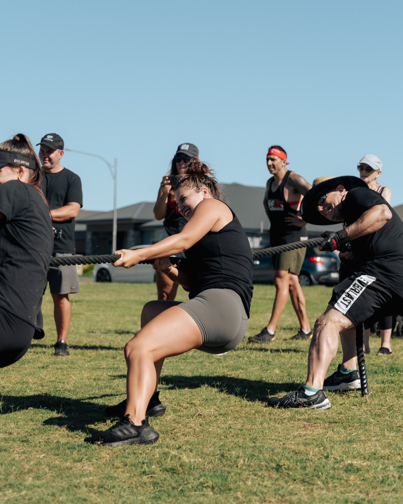People playing tug-of-war on grass on a sunny day. They are pulling hard on a rope.