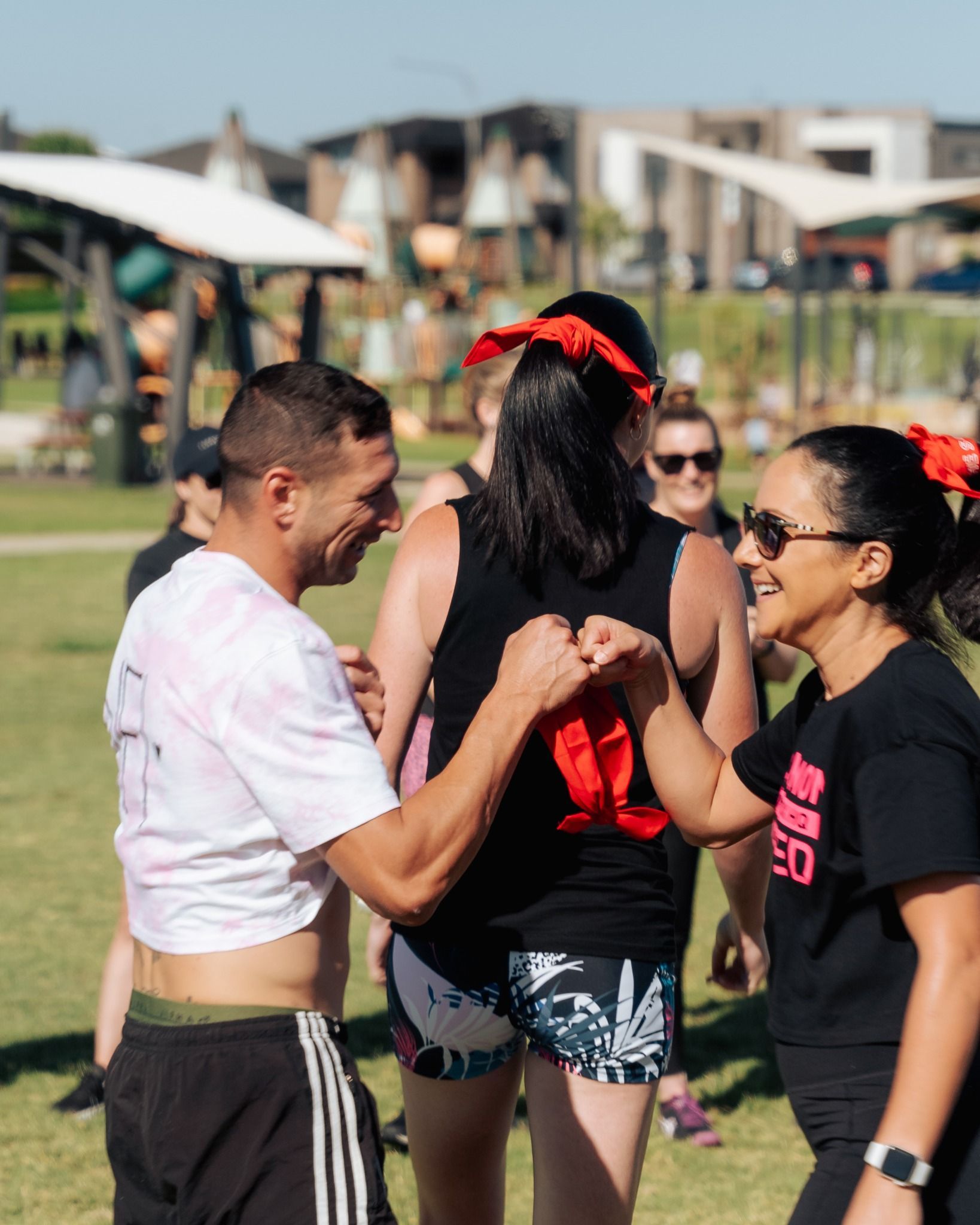 People fist bump outdoors, wearing activewear; sunny day.