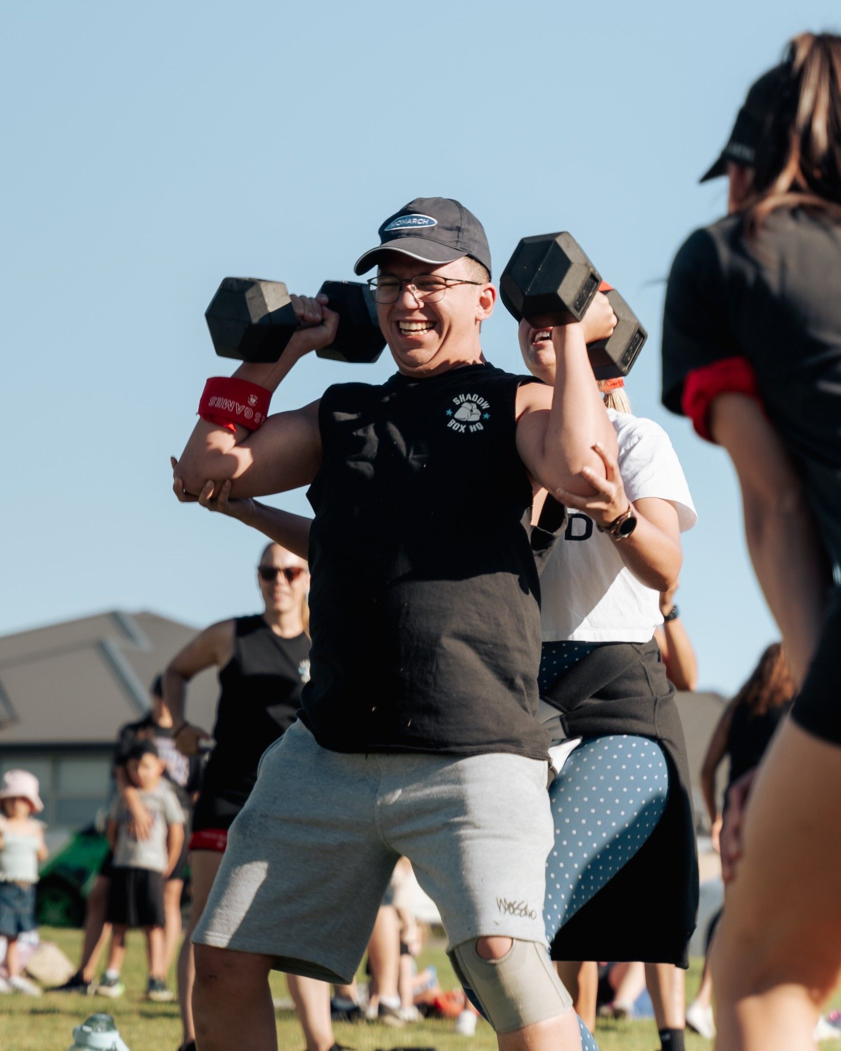 Man in black shirt lifting dumbbells during outdoor fitness class.