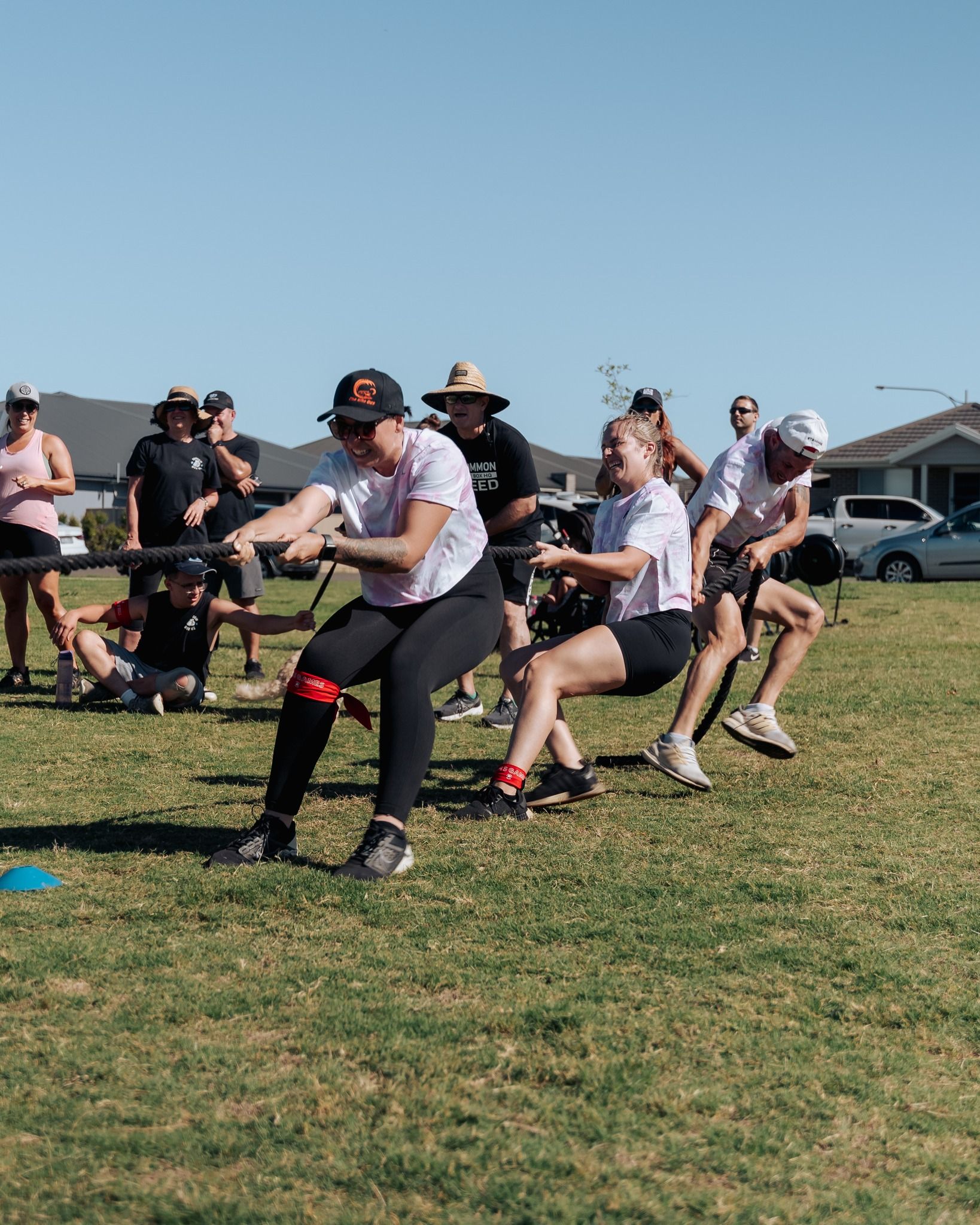 People pulling a rope in a tug-of-war game on a grassy field on a sunny day.