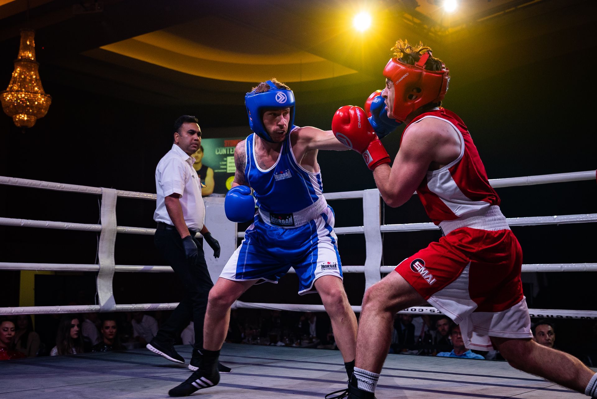 Two boxers in blue and red gear in a ring, throwing punches with a referee.