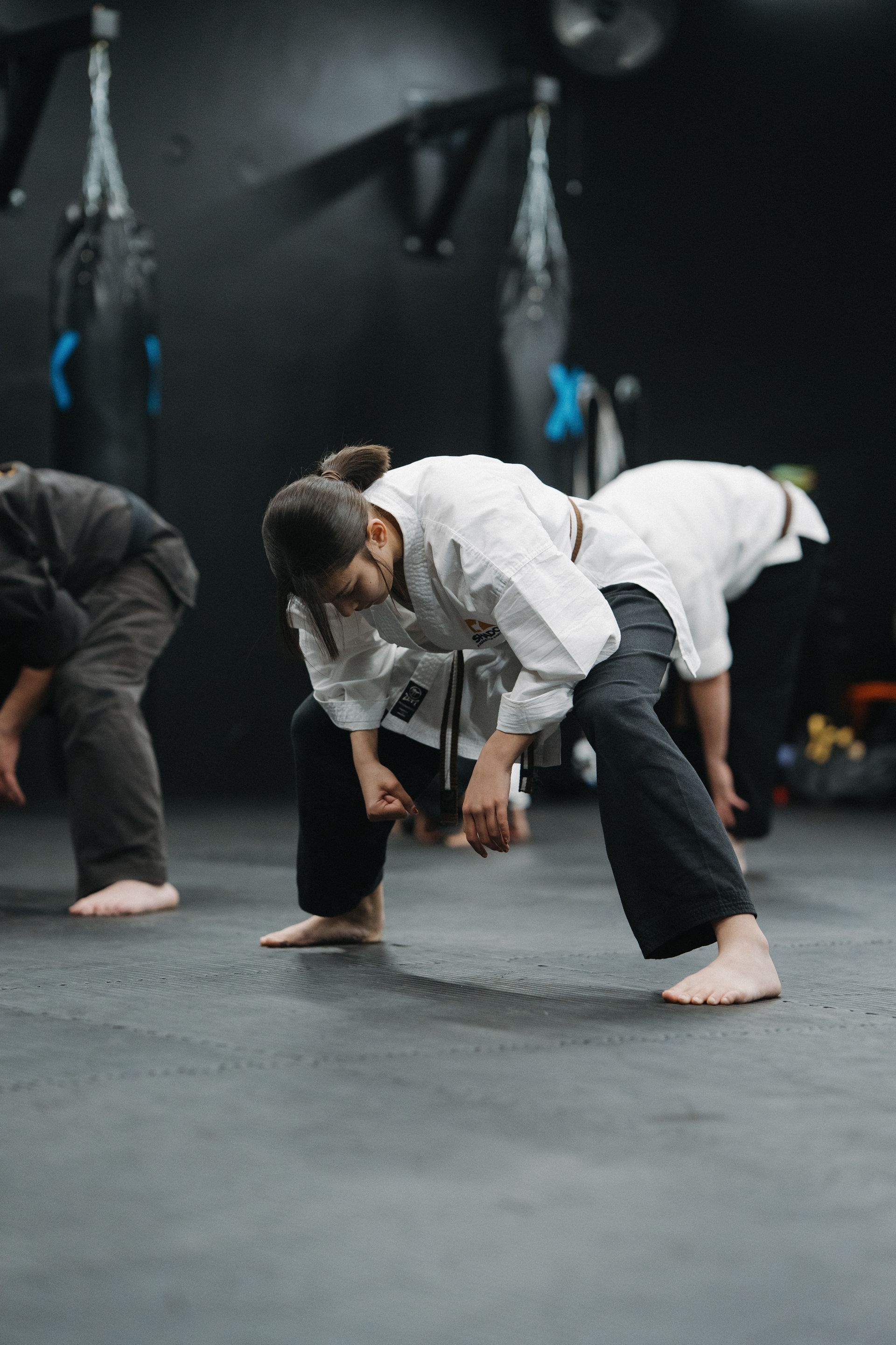 People in karate uniforms stretching on a dark gym floor.