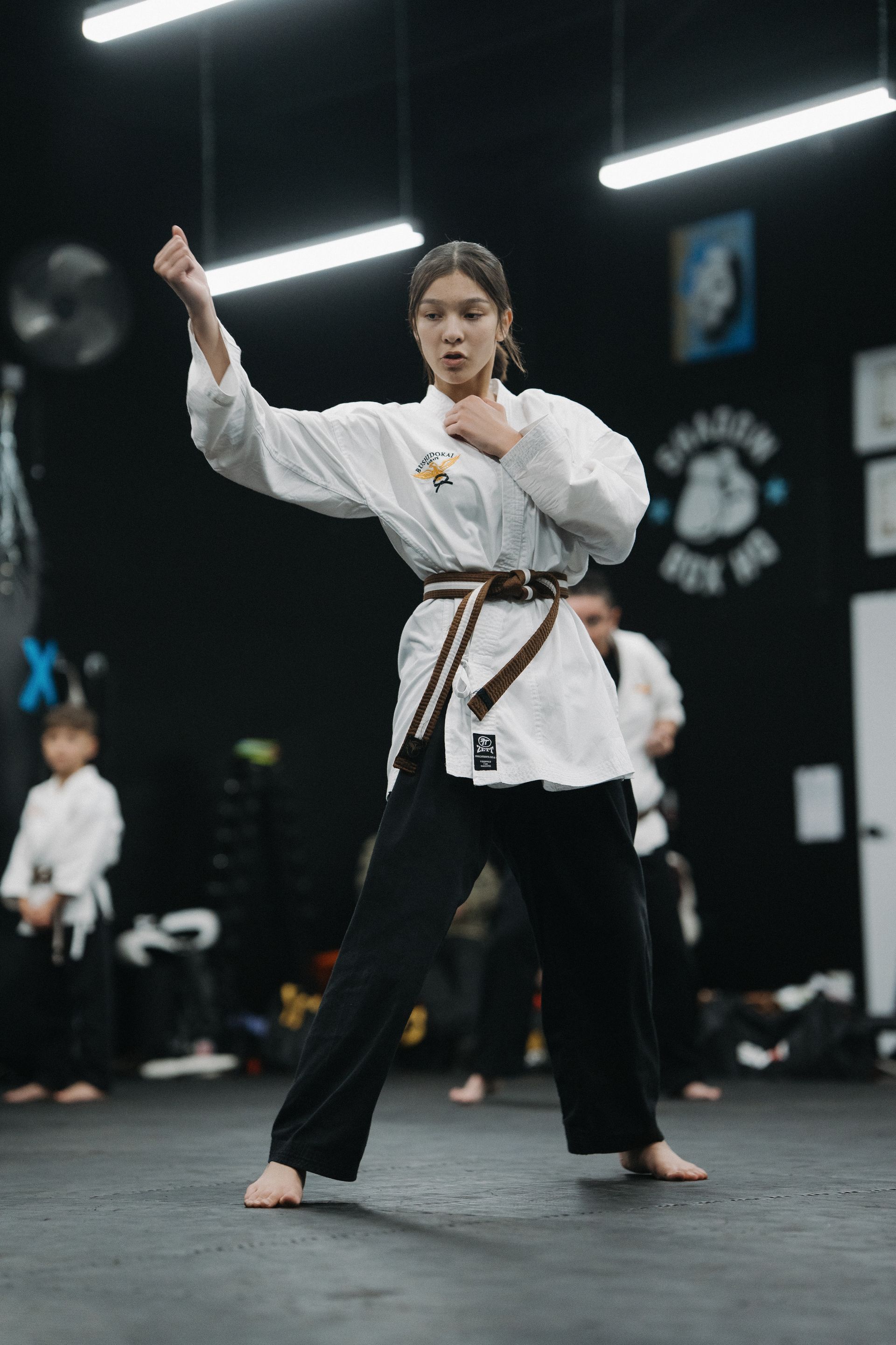 Woman in karate uniform performs a punch, brown belt, training dojo.