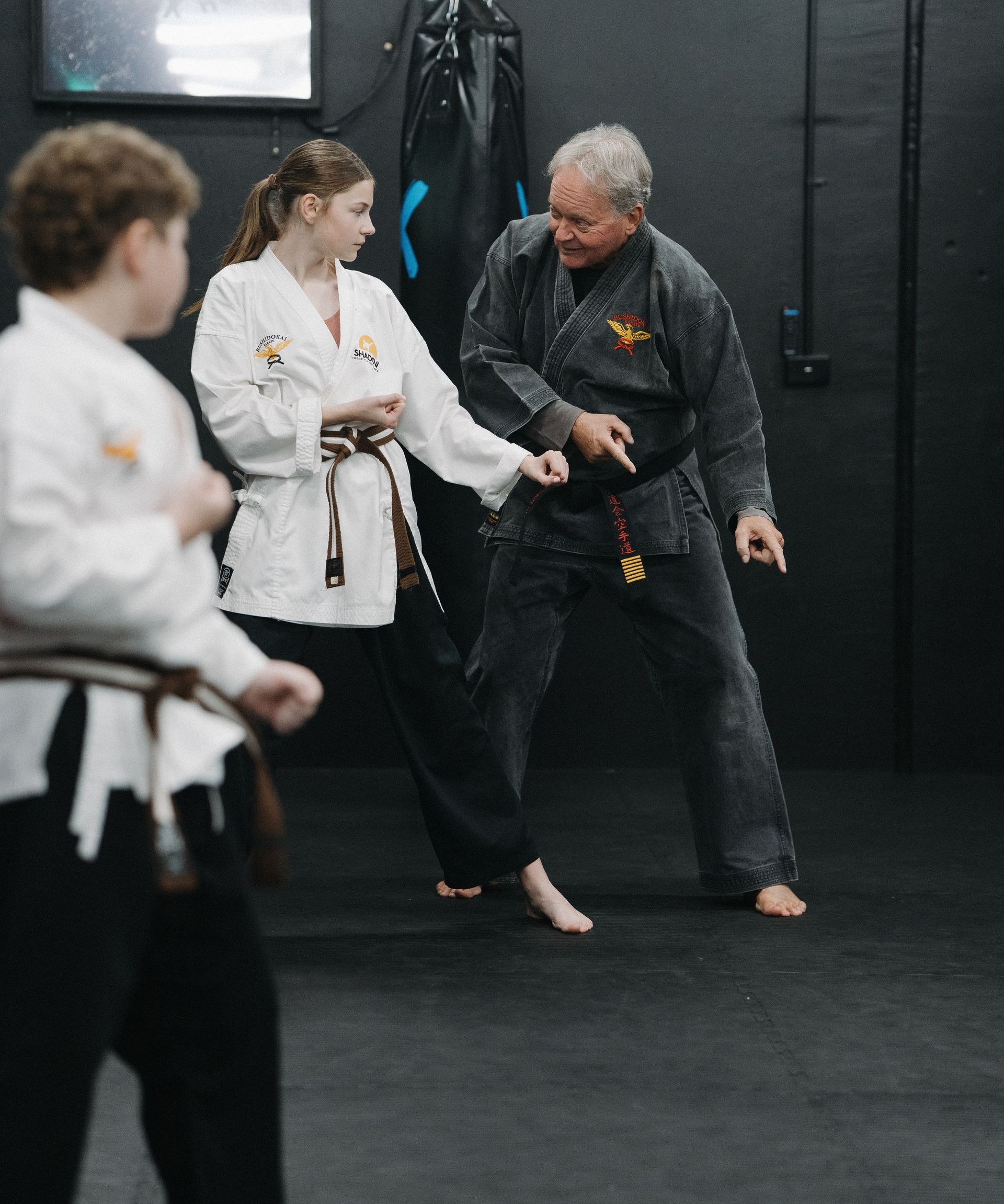 Martial arts class: instructor demonstrating moves to two students in a dark room. All wear uniforms.