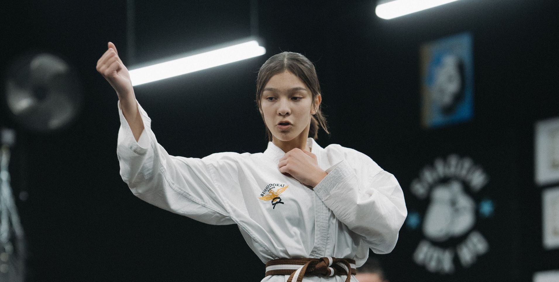 Woman in a karate gi with a brown belt, performing a karate stance in a dojo.