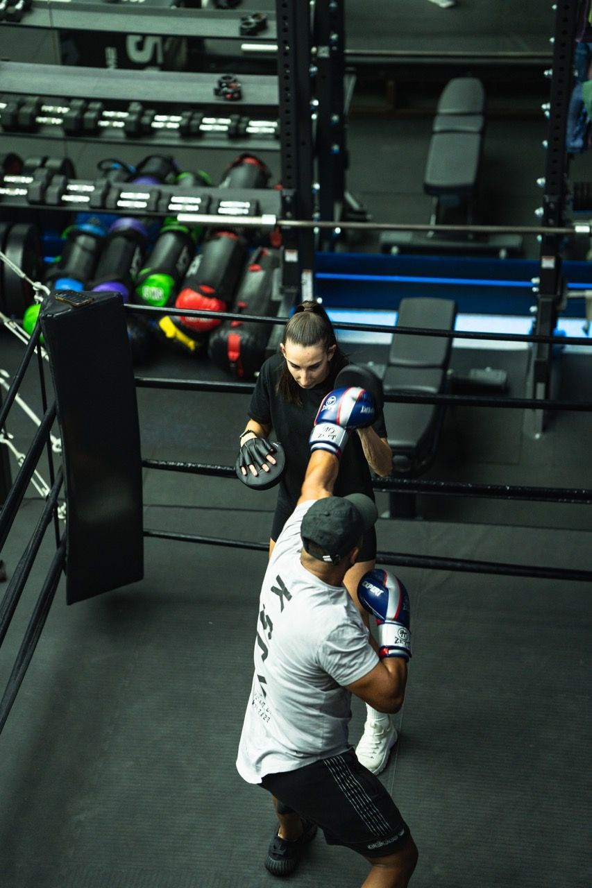 Boxer practicing with a trainer in a boxing ring. Trainer holds pads as boxer throws a punch. Gym setting.