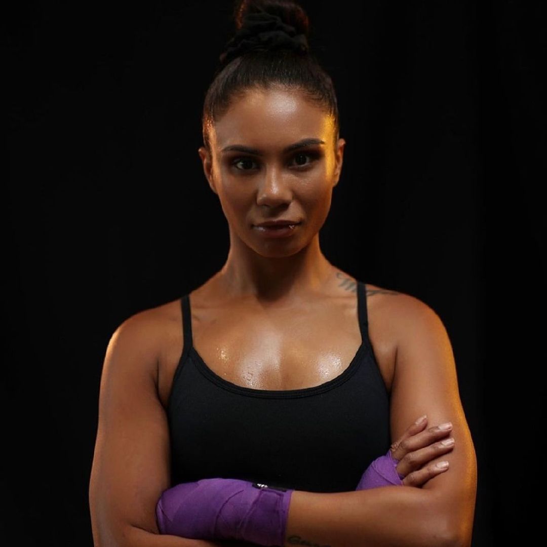 Boxer with arms crossed, wrapped in purple tape, looking forward, black background.