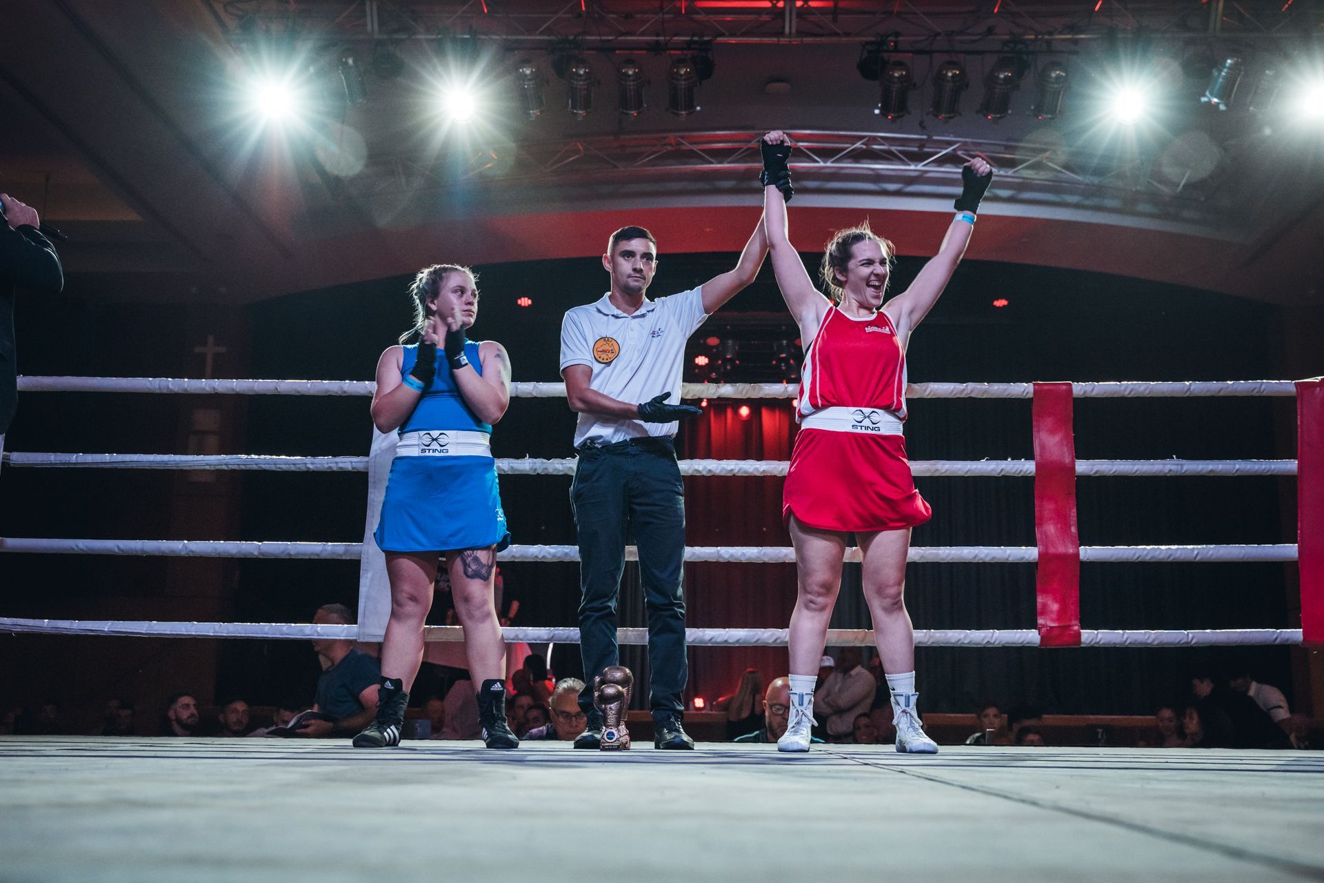 Boxer in red, arms raised in victory, next to a defeated boxer in blue, in a boxing ring.