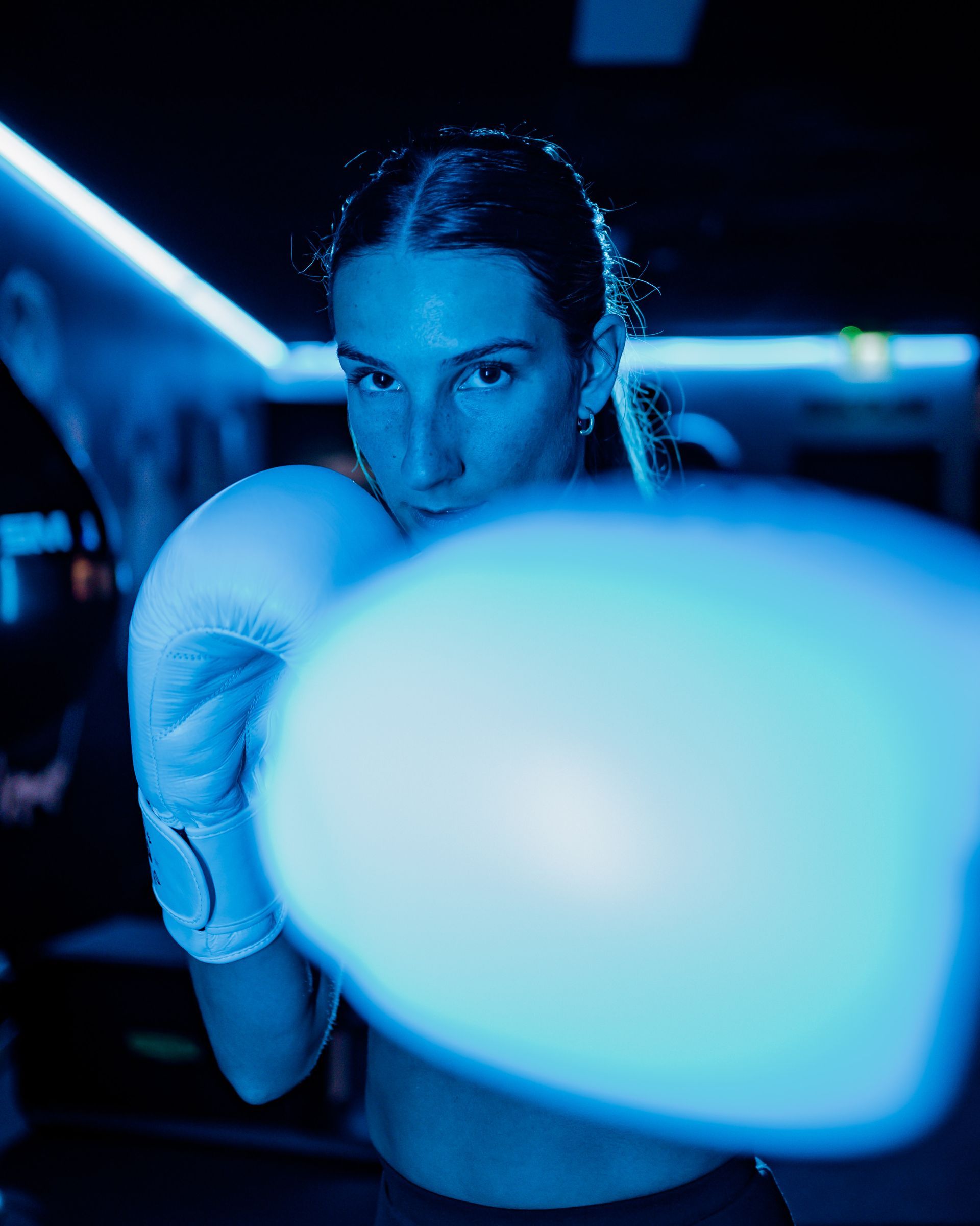 Woman in boxing gloves throwing a punch in a blue-lit gym.