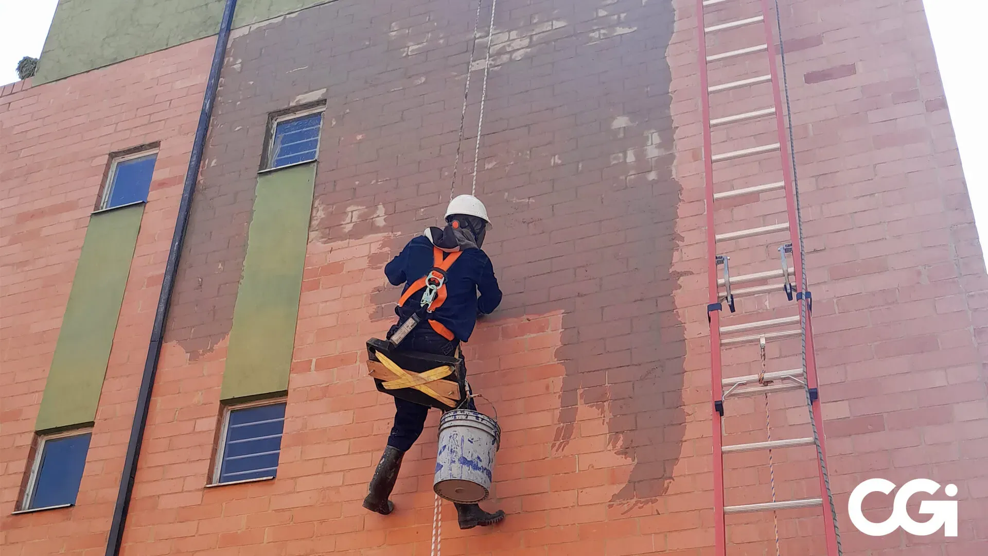 Obrero de la construcción con arnés aplicando estuco a la pared de ladrillo de un edificio.