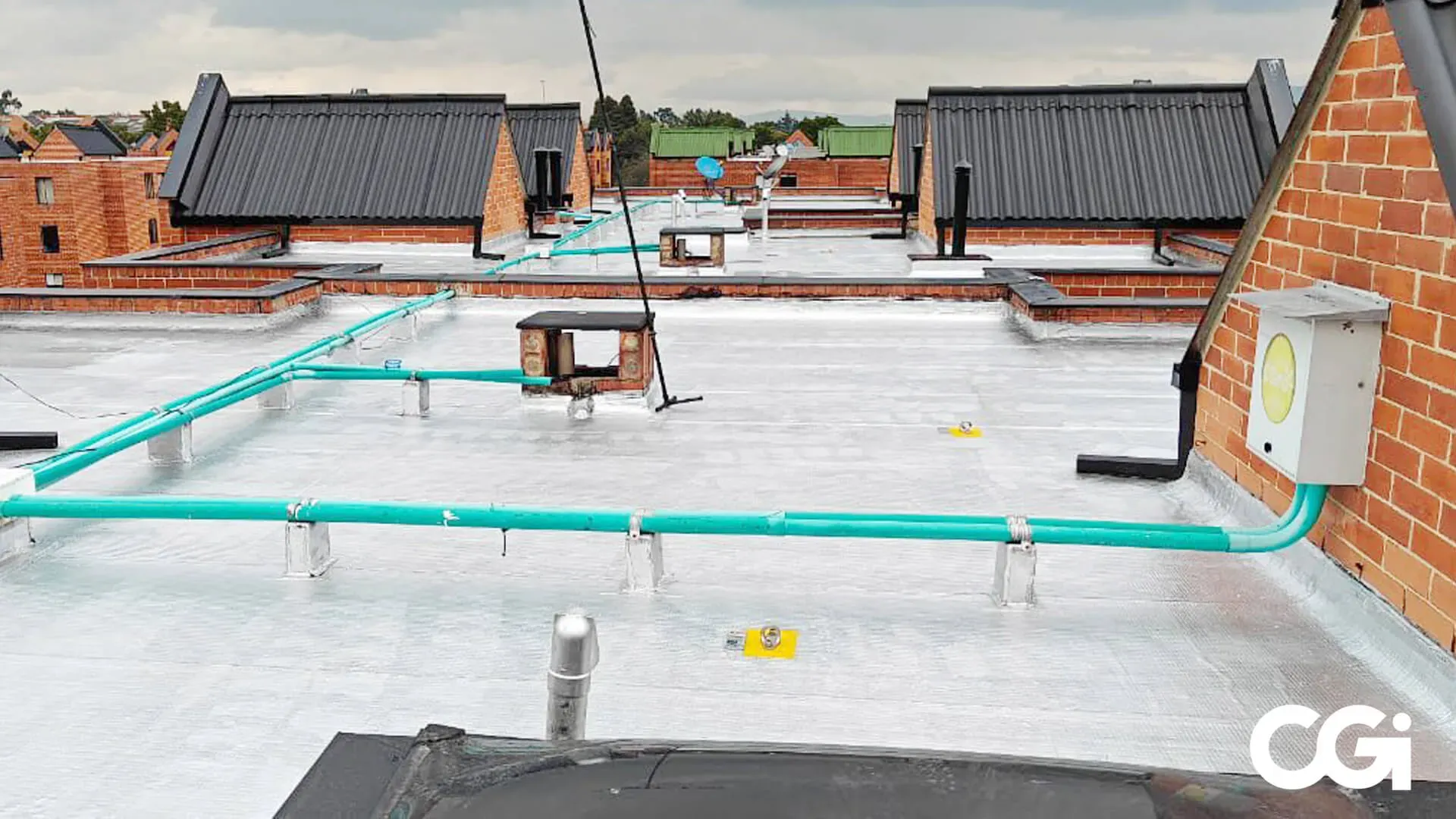 Azotea con tuberías de color verde azulado, cuadro eléctrico y chimeneas de ladrillo; cielo nublado.
