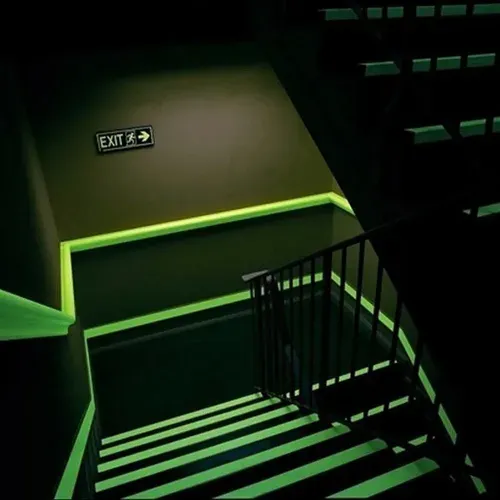 Marcas y letreros de salida de emergencia de color verde brillante en una escalera en un edificio oscuro.