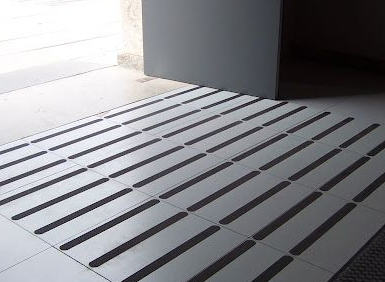 Pavimento táctil con barras lineales elevadas que conducen a una puerta, para la navegación con discapacidad visual.