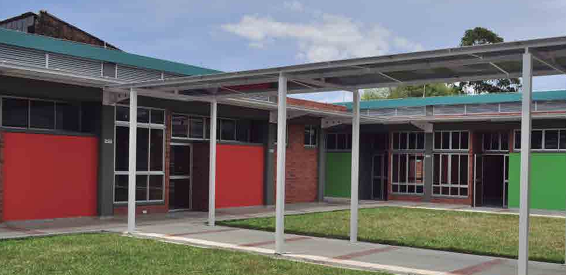 Persona que pinta una pared de ladrillos desde una escalera, vistiendo casco y ropa de trabajo oscura.