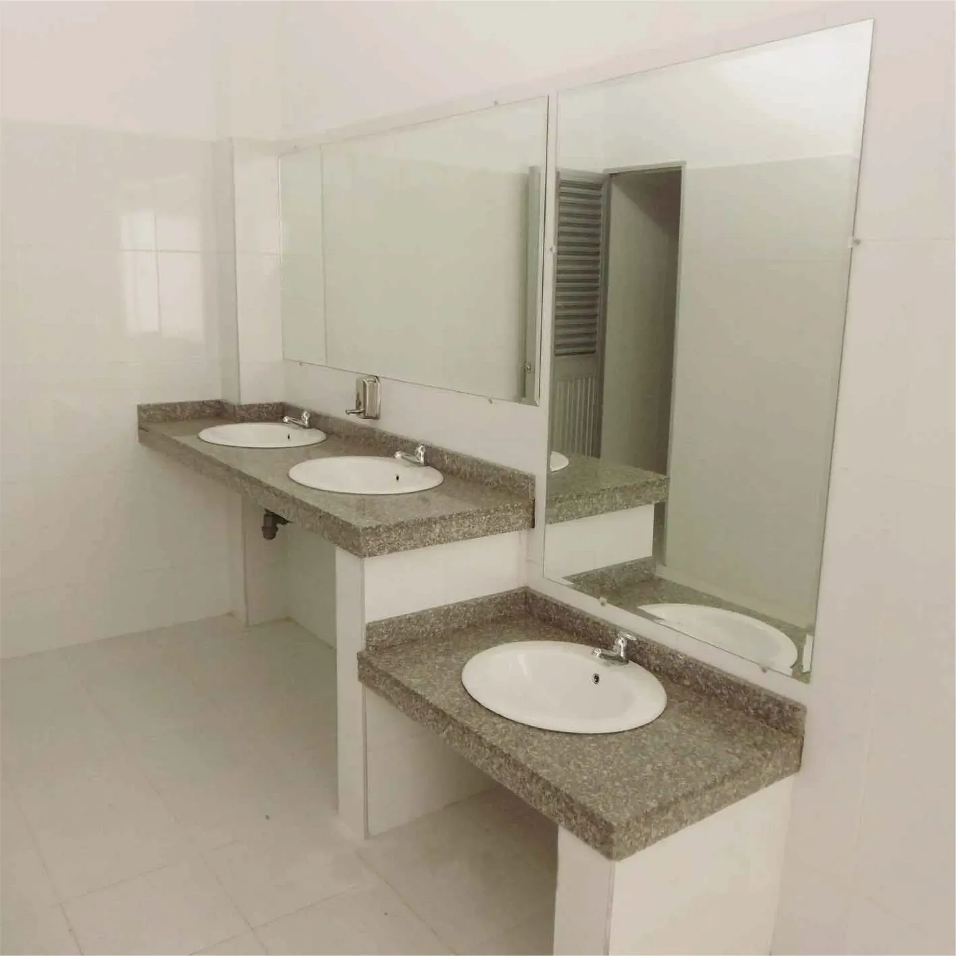 Baño público con tres lavabos, espejos y paredes blancas.
