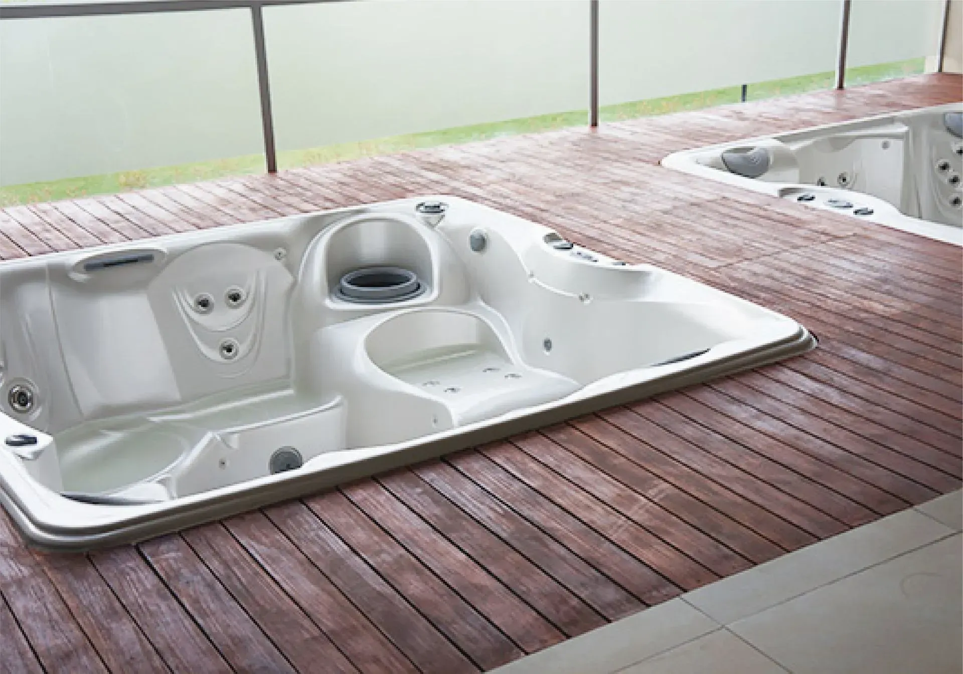 Dos jacuzzis blancos sobre una terraza de madera junto a una barandilla de cristal, con vistas a la vegetación.