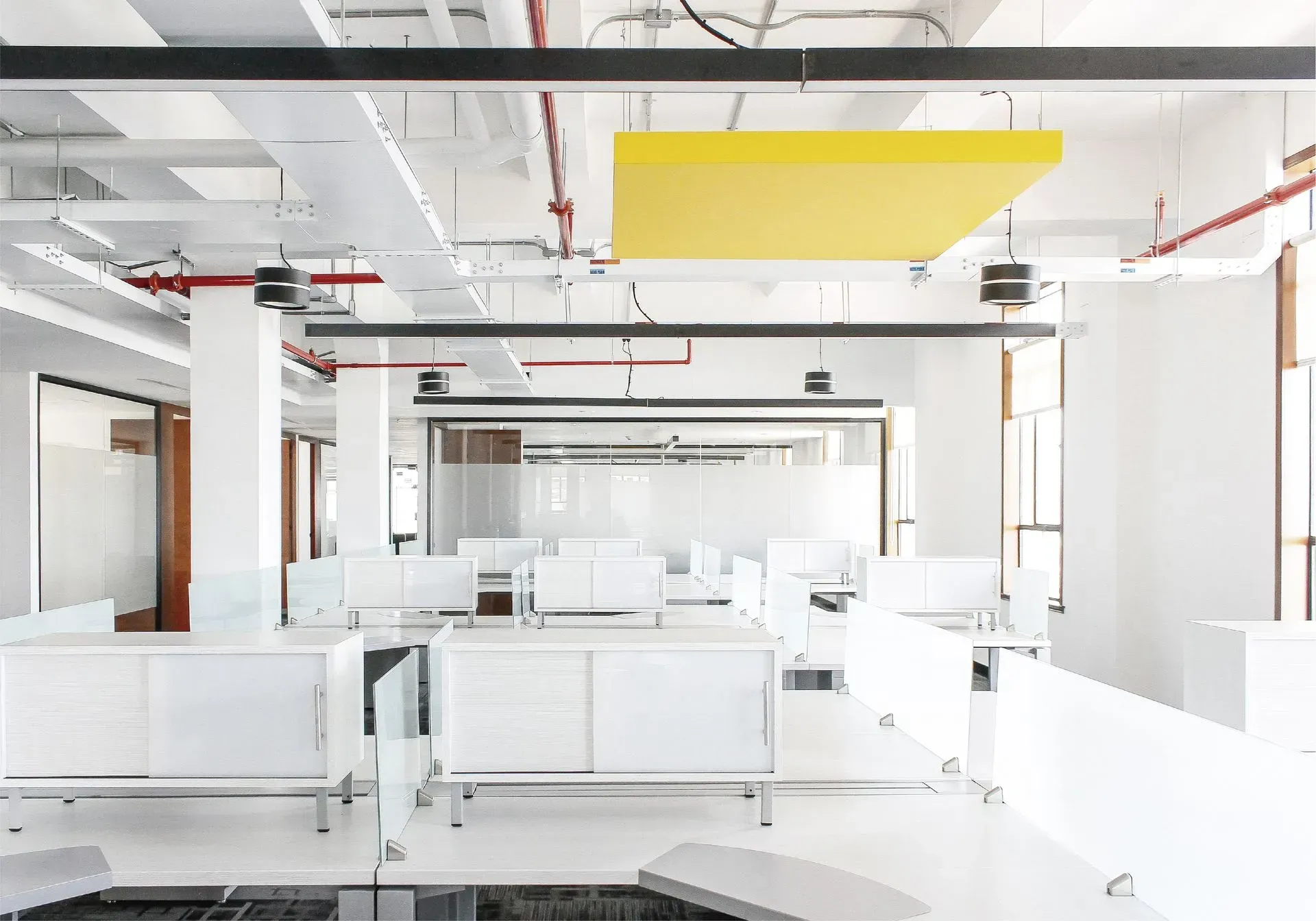 Espacio de oficina moderno y luminoso con escritorios y paredes blancos y un panel de sonido amarillo.