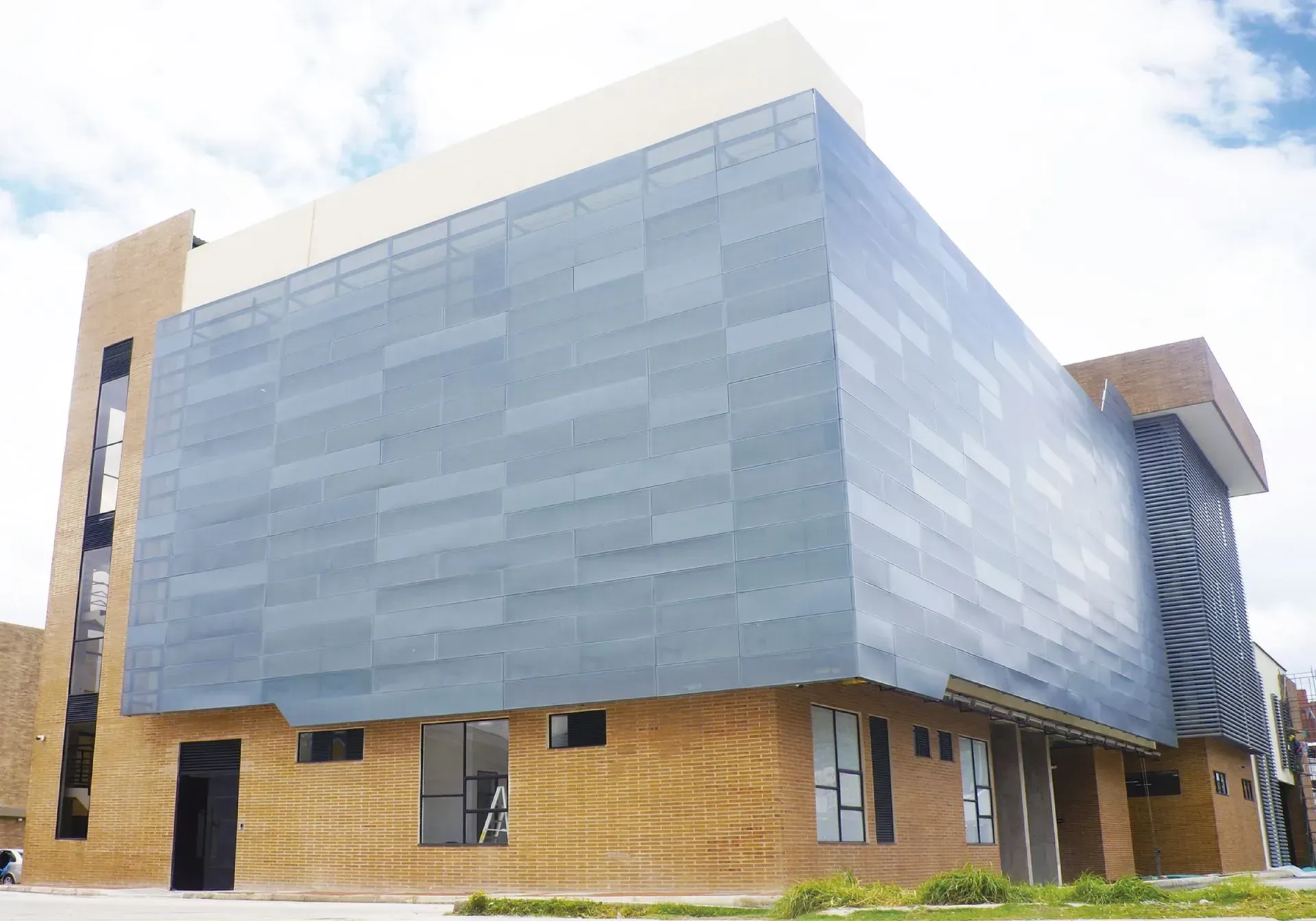 Edificio moderno con fachada de metal gris, ladrillo color canela y ventanas contra un cielo nublado.