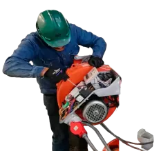 Persona con equipo de seguridad reparando máquina naranja, utilizando un destornillador.