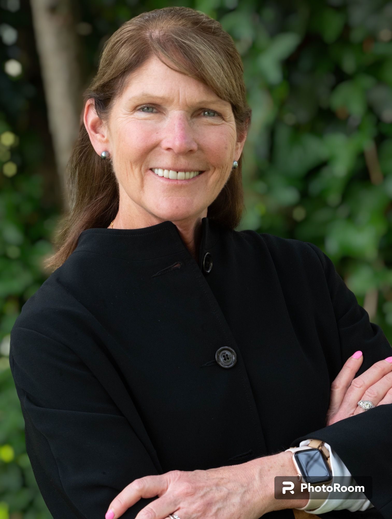 A woman in a black coat is smiling with her arms crossed