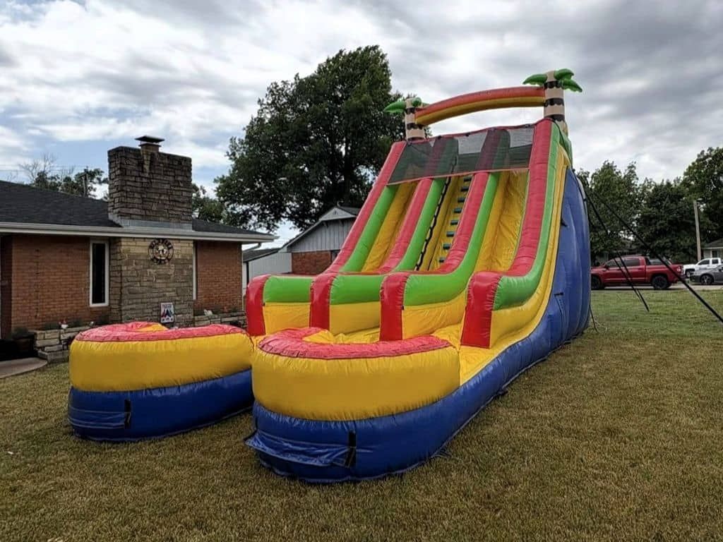 Colorful inflatable bounce slide on a grassy yard beside a brick house under a cloudy sky