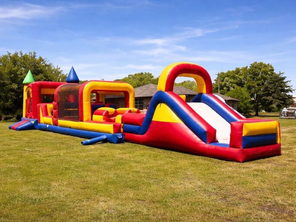 Blue inflatable triple slide with palm-tree decorations on a grassy field under a clear sky