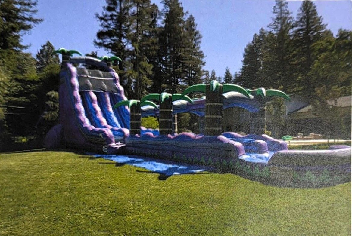 Colorful inflatable bounce slide on a grassy yard beside a brick house under a cloudy sky