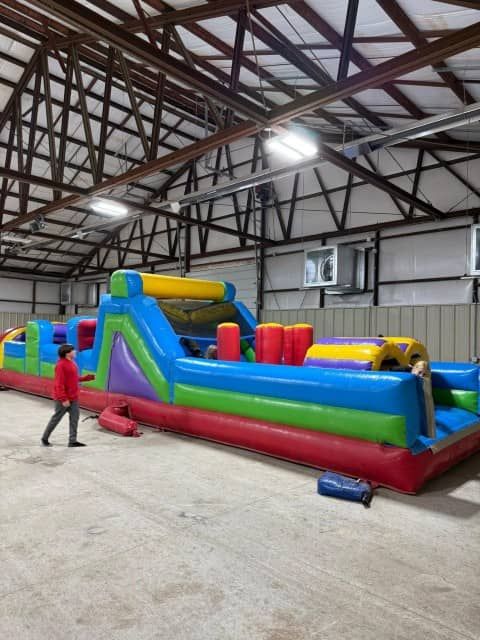 Colorful inflatable obstacle course inside a fairgrounds building in Blackwell, OK, with a person standing beside it.