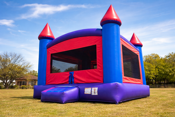 Blue and red inflatable castle bounce house on green grass under a blue sky.