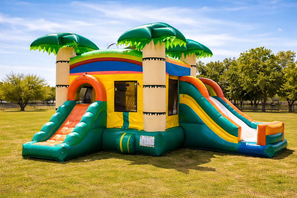 Colorful inflatable bounce house with slides and palm tree decorations in a grassy field.