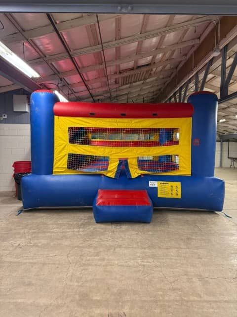 Blue and red inflatable bounce house with yellow mesh, indoors on a concrete floor
