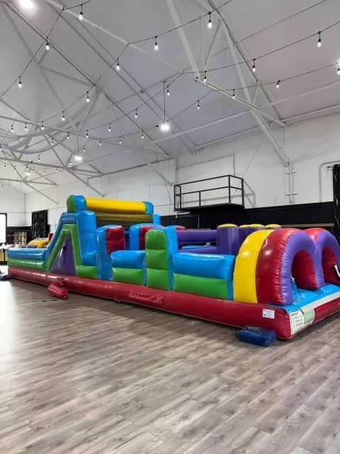 Large colorful inflatable obstacle course inside a gymnasium with a high ceiling and wood floor
