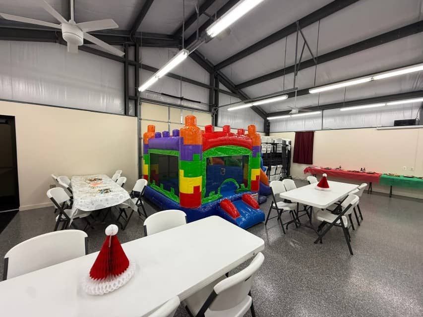 Indoor party room with tables and a colorful bounce house under a metal ceiling