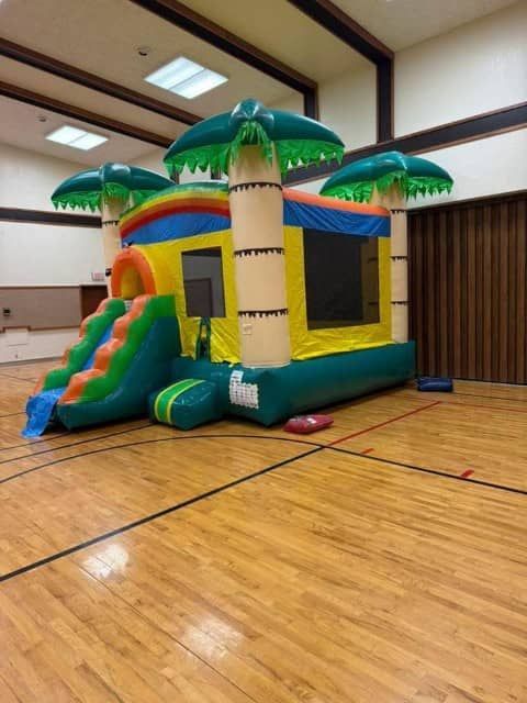 Colorful tropical bounce house inside a gymnasium with wooden floor and high ceiling