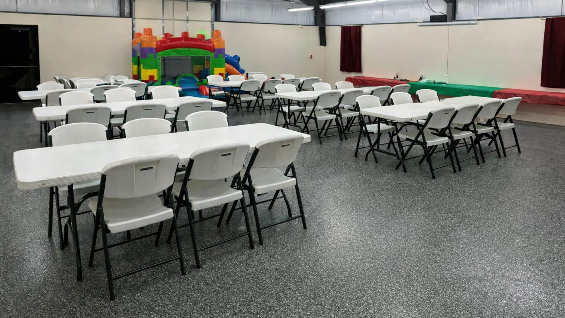 Tables and chairs arranged in a large room with a bouncy castle in the background.