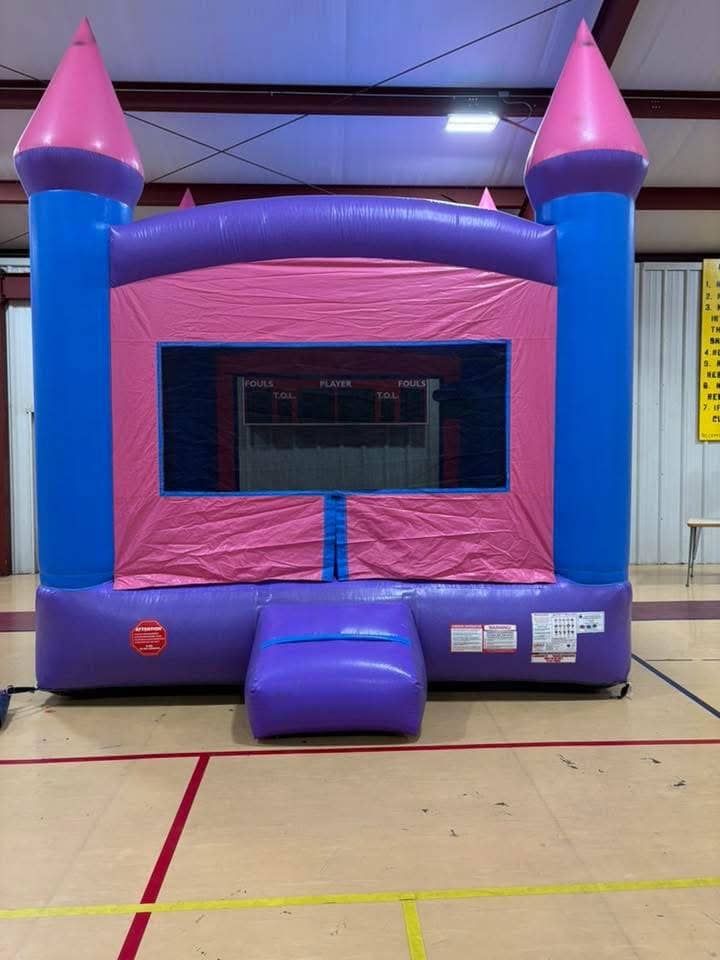 Pink and blue inflatable bounce house indoors with a front entrance and window