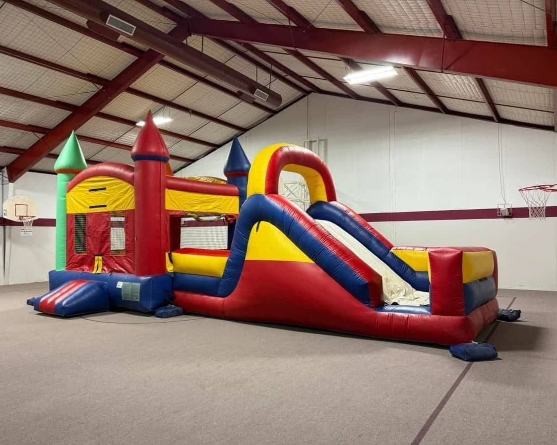 Colorful inflatable bounce slide on a grassy yard beside a brick house under a cloudy sky