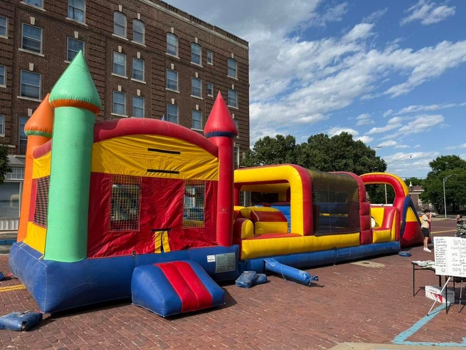 Colorful inflatable bounce house on a brick plaza beside a brick building under a blue sky.