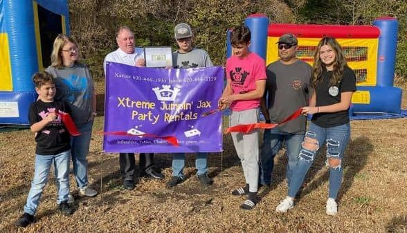 Group holding a purple “Xtreme Party Rentals” banner in front of a colorful bounce house outdoors