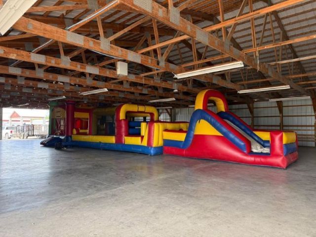Colorful inflatable obstacle course inside a large wooden pavilion with a concrete floor