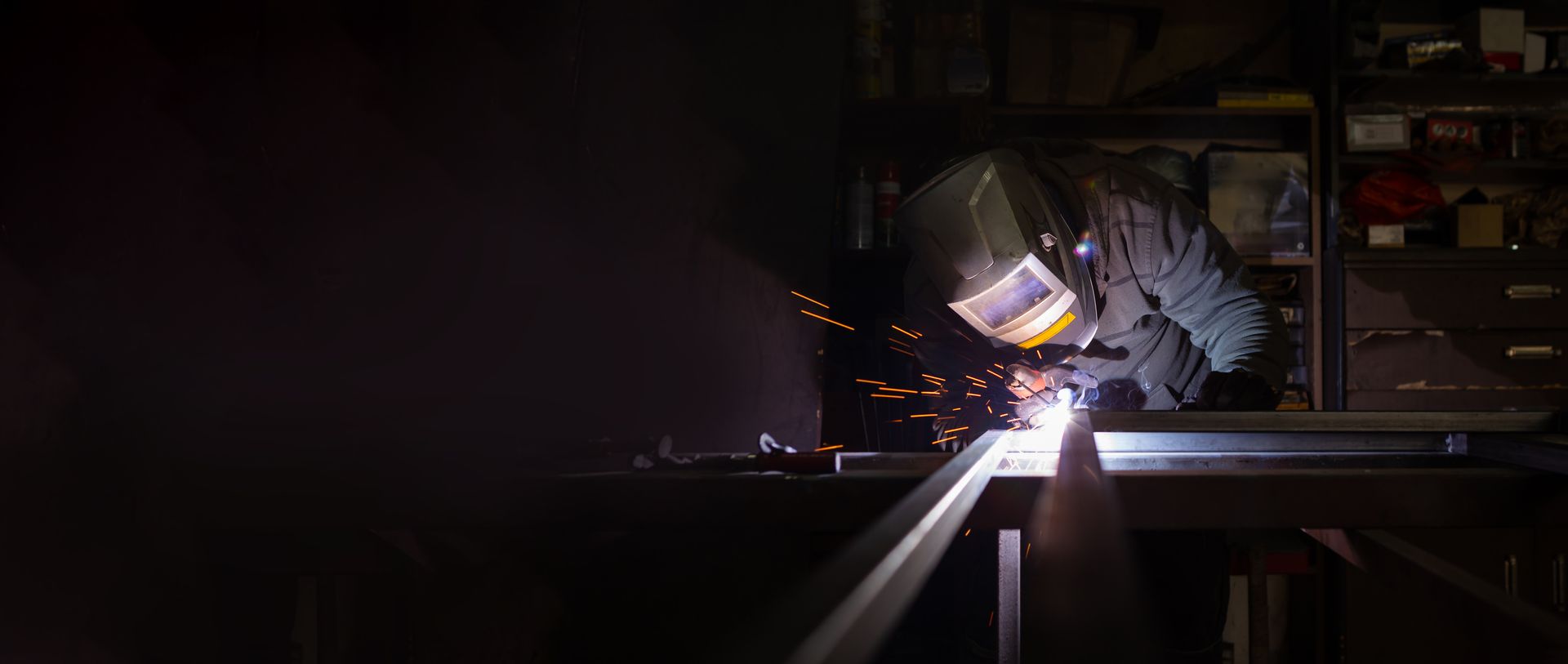 He holds a welding machine in his hand and welds the metal structure.