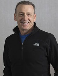 A man wearing a black jacket and a blue shirt is smiling for the camera.