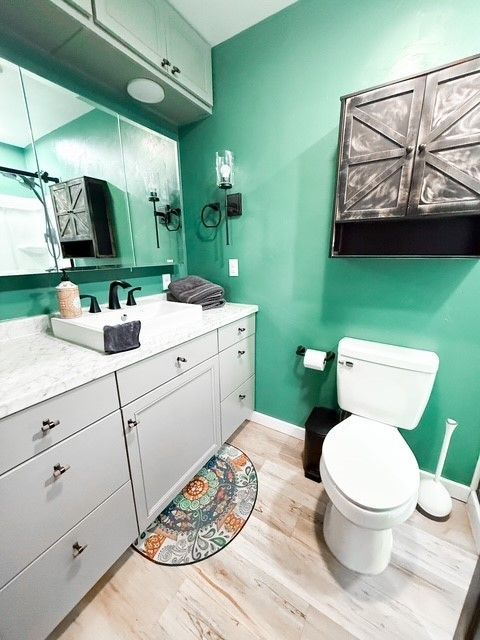 Bathroom with green walls, gray vanity, toilet, and decorative cabinet.