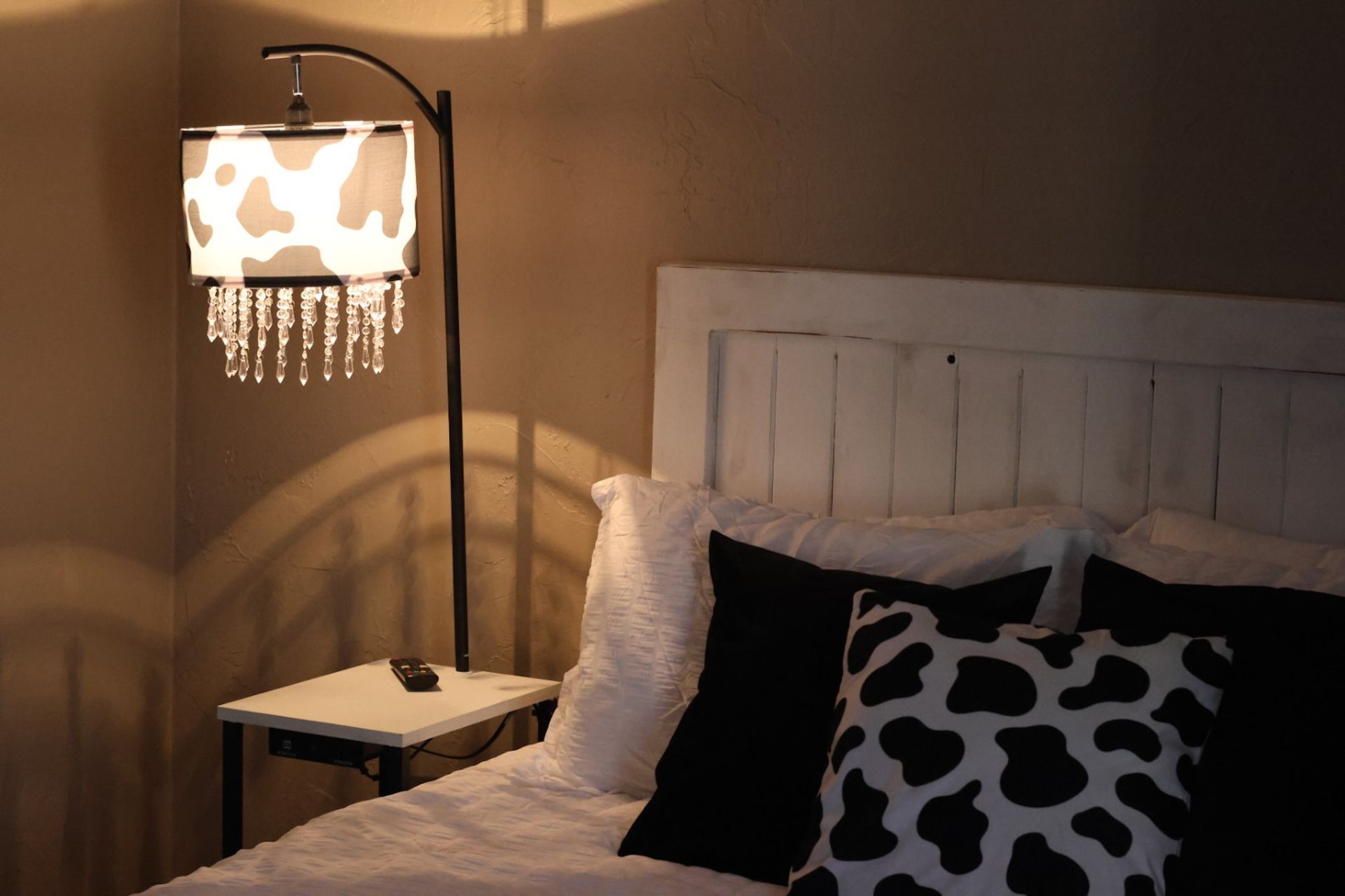 Bedroom corner with cow-print lamp and pillow, white headboard, and black pillows.