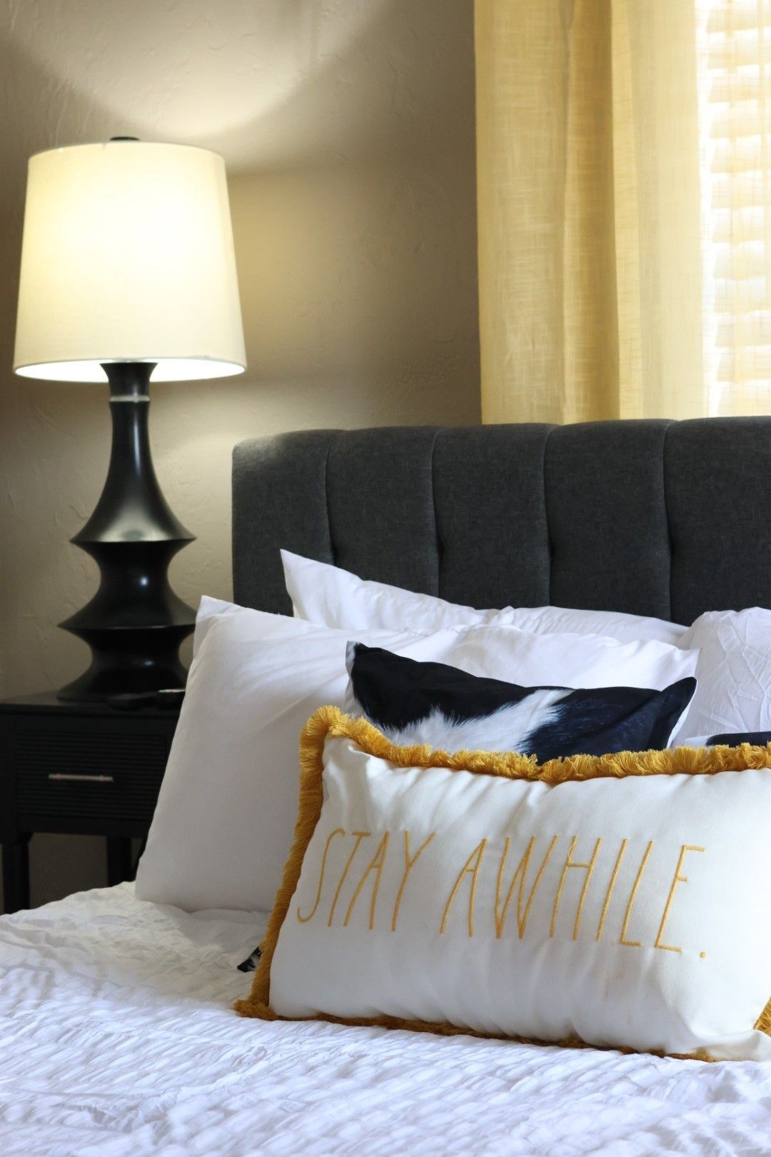 Bedroom with upholstered headboard, white bedding, pillows, lamp on nightstand. 