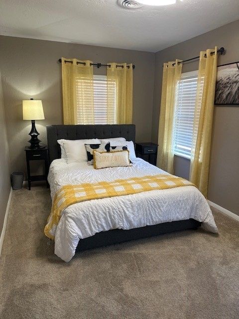 Bedroom with queen bed, gray walls, yellow curtains, and black bedside tables.